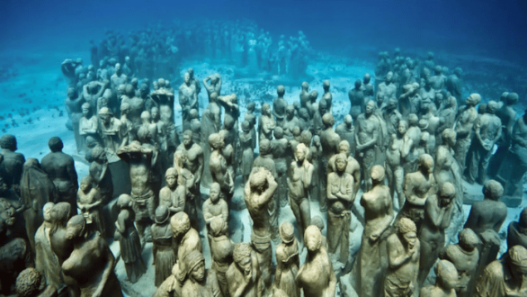 Esculturas del Museo Subacuático de Arte de Cancún cubiertas por organismos marinos y rodeadas de peces