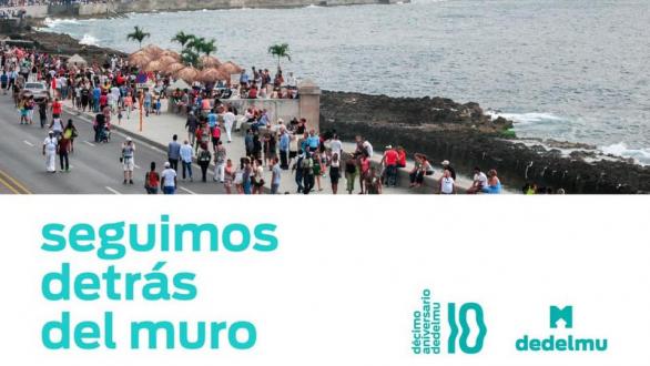 cartel por el décimo aniversario de detrás del muro. personas caminan entre las obras de arte del MAlecón habanero